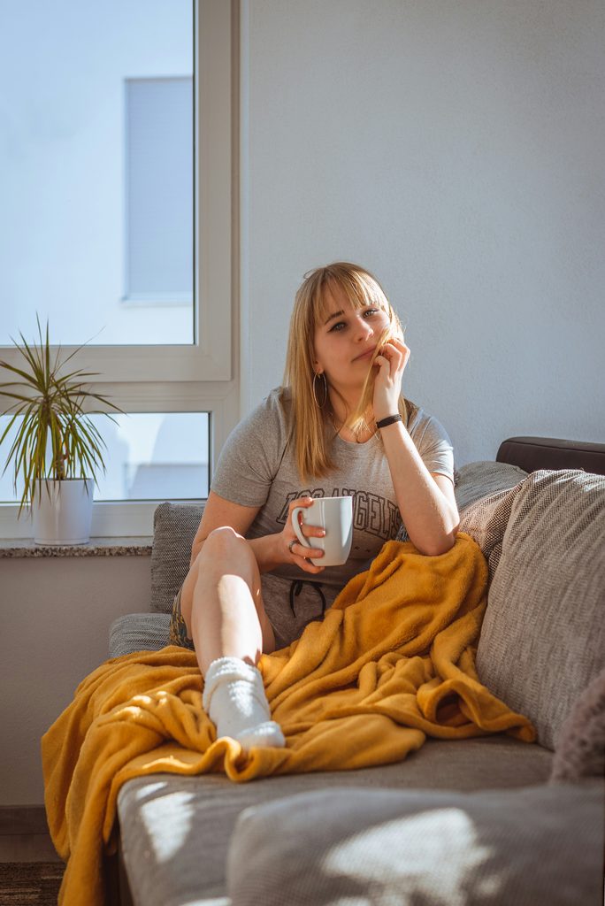 chica sentada en el sofá con una taza de café sonriendo sin ansiedad con la terapia de PsicoSerenidad en Almería